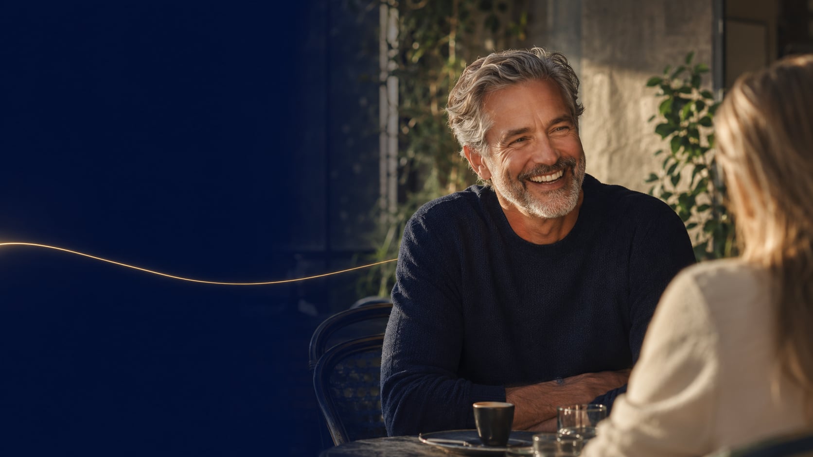 Pessoa madura sorrindo com naturalidade numa conversa à mesa de café.